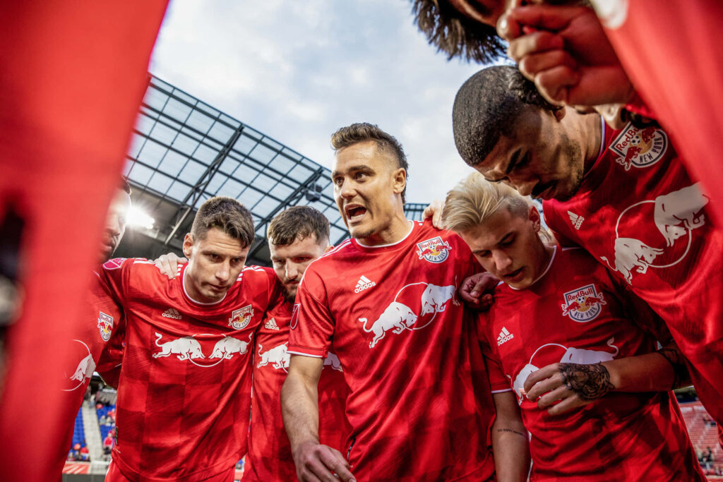 Athlete Aaron Long and New York Red Bulls teammates huddle in red jerseys showing team unity Wallpaper