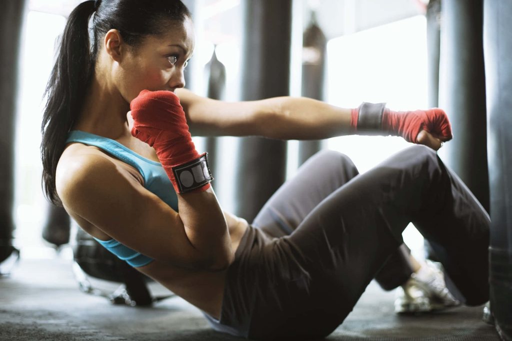 Athletic woman in blue tank top with red boxing wraps doing core workout gym wallpaper background