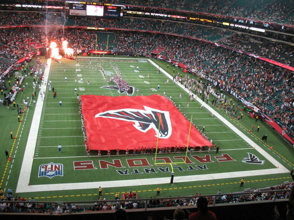 Atlanta Falcons team flag on field with flames erupting in packed stadium electrifying scene Wallpaper