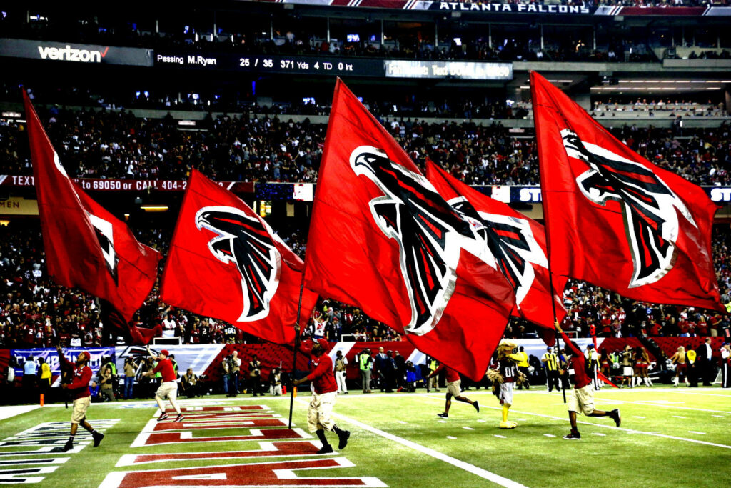 Atlanta Falcons flag bearers running on field at packed stadium showing game day excitement Wallpaper