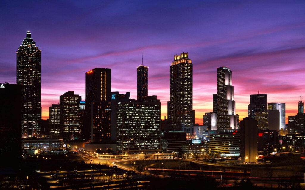 Atlanta skyline at dusk with illuminated high-rise buildings and a dramatic sunset background Wallpaper