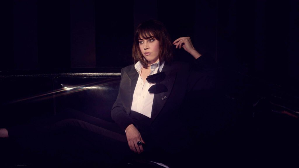 Aubrey Plaza confident in sharp suit moody dramatic wallpaper background stylish portrait