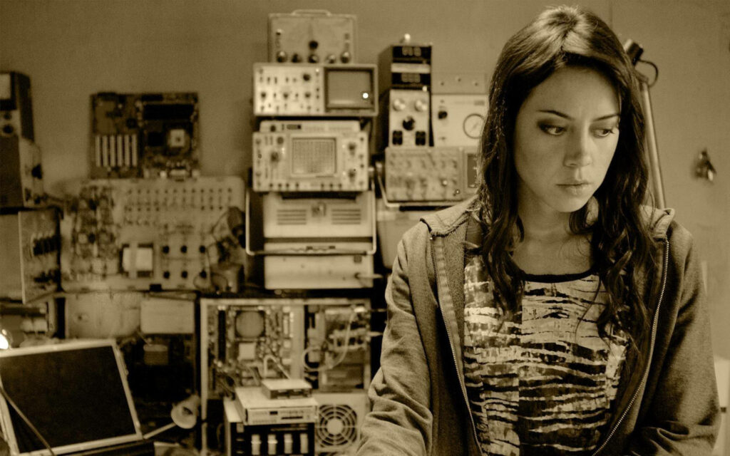 Aubrey Plaza in thoughtful pose in vintage electronics lab scene from Dilemma wallpaper background