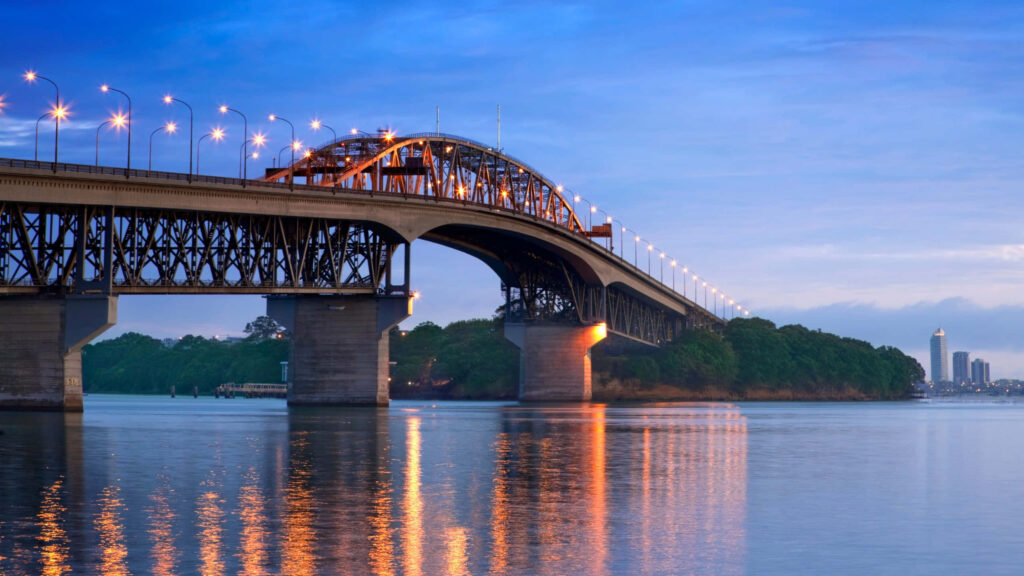Auckland Harbour Bridge at dusk glowing with warm lights reflecting on calm evening waters wallpaper