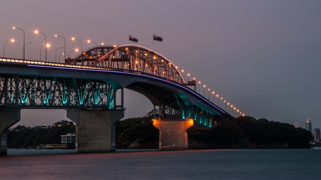 Auckland Harbour Bridge illuminated at twilight reflecting over calm water scenic wallpaper