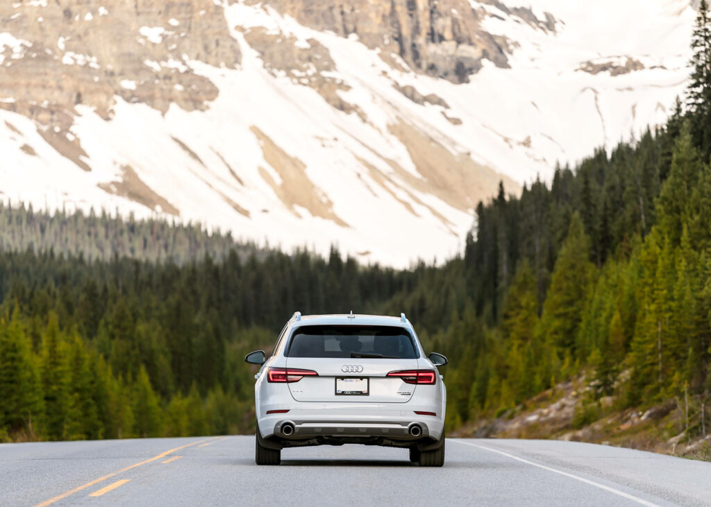 Audi A4 rear view driving on scenic mountain road with green forests and snow-capped peaks Wallpaper