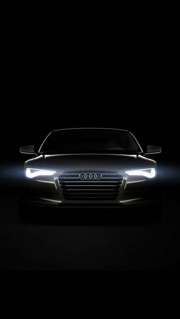 Front view of sleek Audi car with glowing headlights emerging from dark wallpaper background