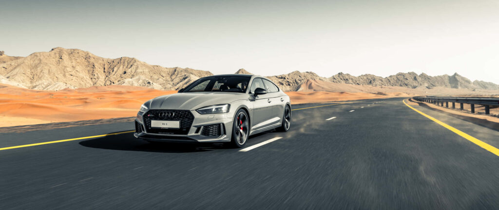 Audi RS sports car driving on open highway with desert mountains luxury performance wallpaper