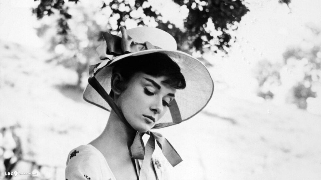 Audrey Hepburn in wide ribbon hat outdoors exuding timeless grace classic Hollywood charm wallpaper