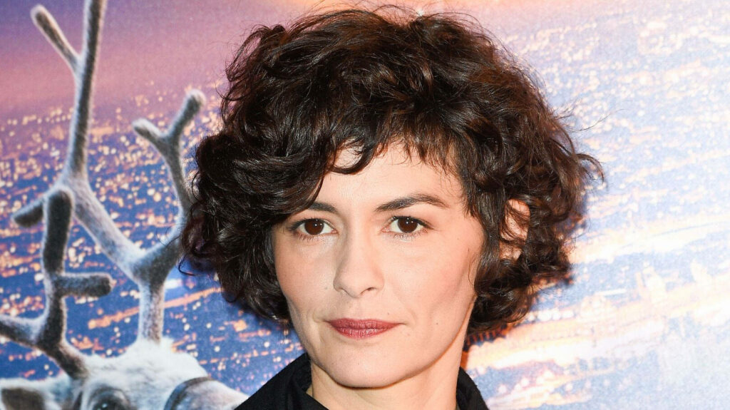Audrey Tautou with curly hair stands against colorful blurred backdrop elegant style wallpaper