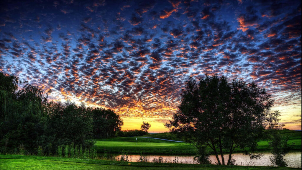 Aerial view of Augusta National Golf Course with green fairways trees pond at sunset sky background Wallpaper