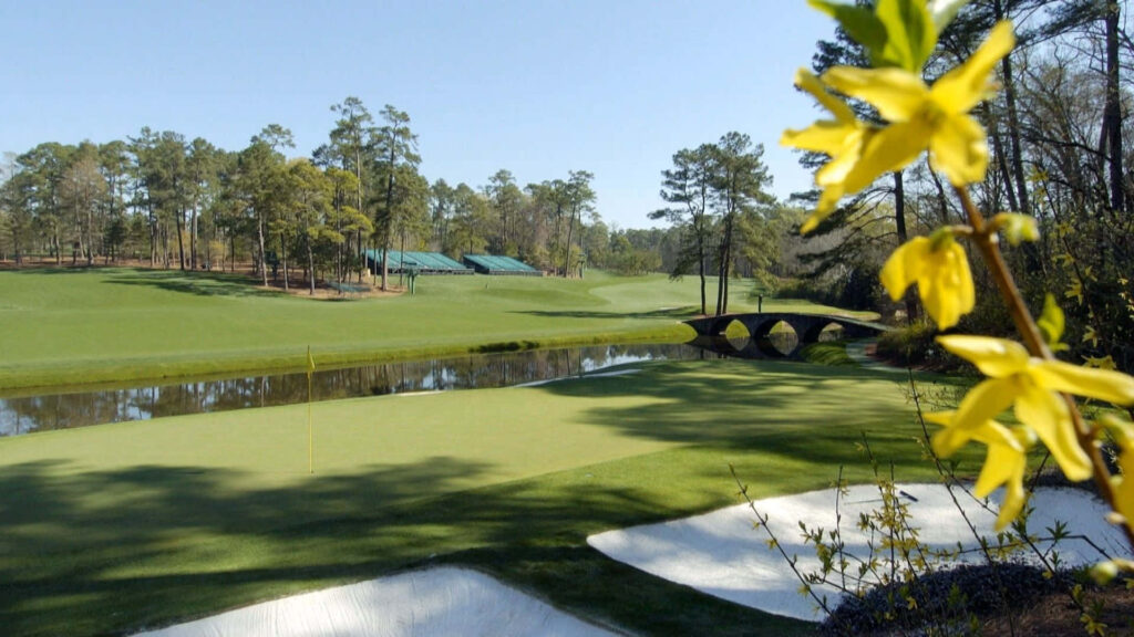 Sunrise over Augusta National Golf Course with green fairways yellow blooms and calm water view Wallpaper