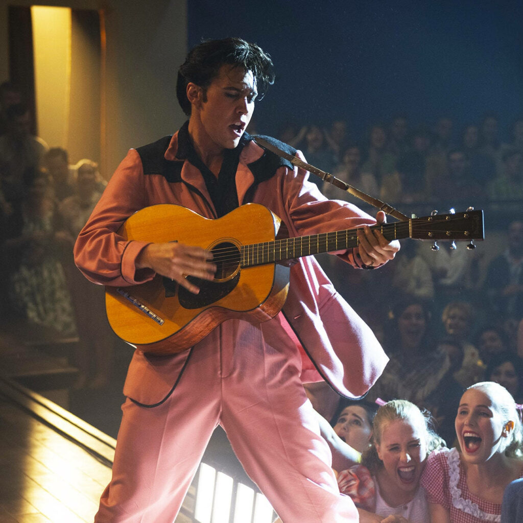 Austin Butler as Elvis Presley playing guitar live in retro pink suit energetic 1950s rock wallpaper