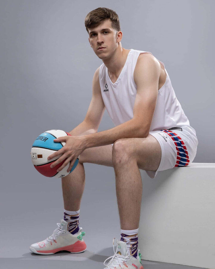 Austin Reaves in basketball uniform holding colorful ball studio portrait with clean wallpaper background