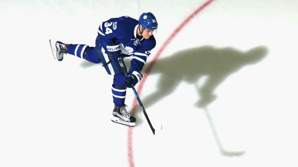 Auston Matthews in Toronto Maple Leafs uniform skating for a powerful hockey shot on ice Wallpaper