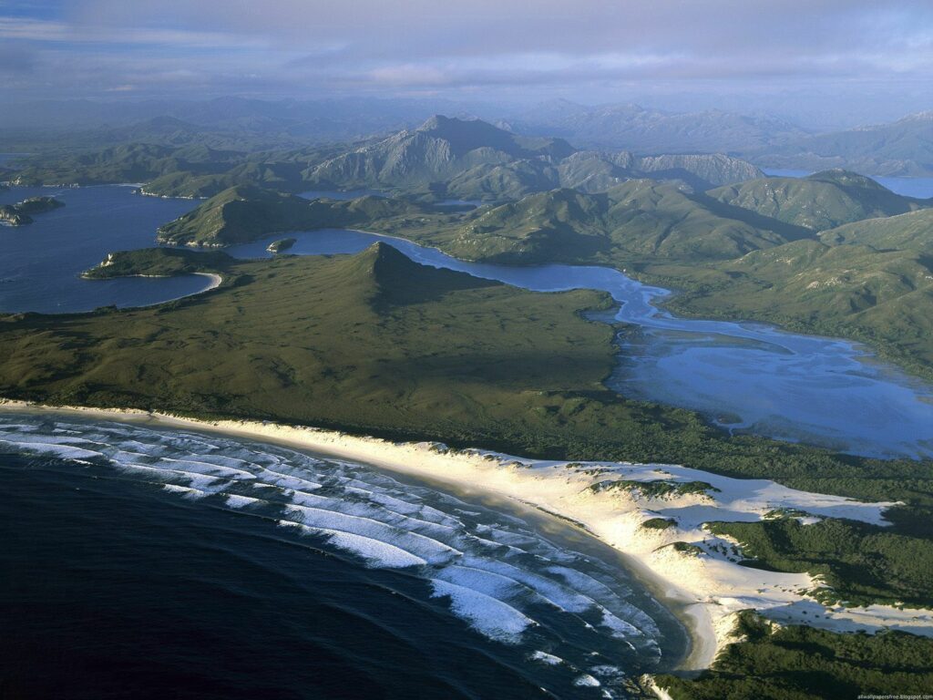 Dramatic Australian coastline with green hills rivers white beaches deep blue sea and misty mountains Wallpaper