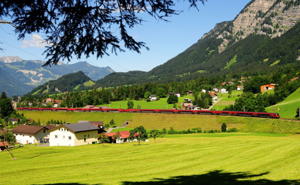 Scenic Austrian countryside with rolling hills red train charming village and majestic mountains wallpaper