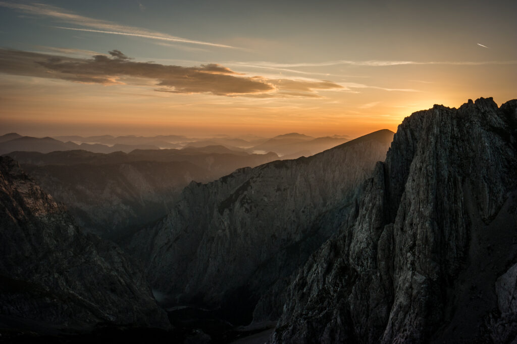 Sunset over rugged Austrian mountain peaks glowing in golden light with misty layers and serene sky Wallpaper