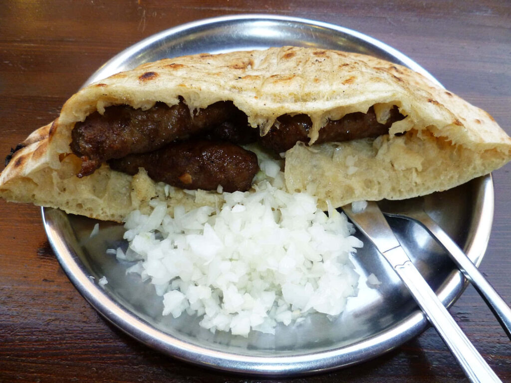 Traditional Balkan cevapi in golden pita bread with fresh onions on metal plate wallpaper background