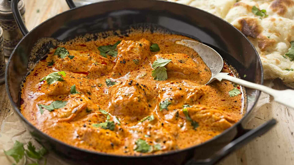 Creamy butter chicken in rustic bowl with cilantro garnish vibrant Indian curry wallpaper background