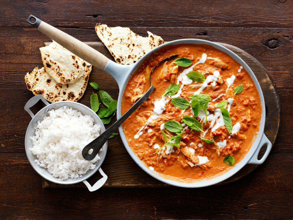 Butter chicken in rustic pan with cream swirl fresh mint naan bread and fluffy white rice background Wallpaper