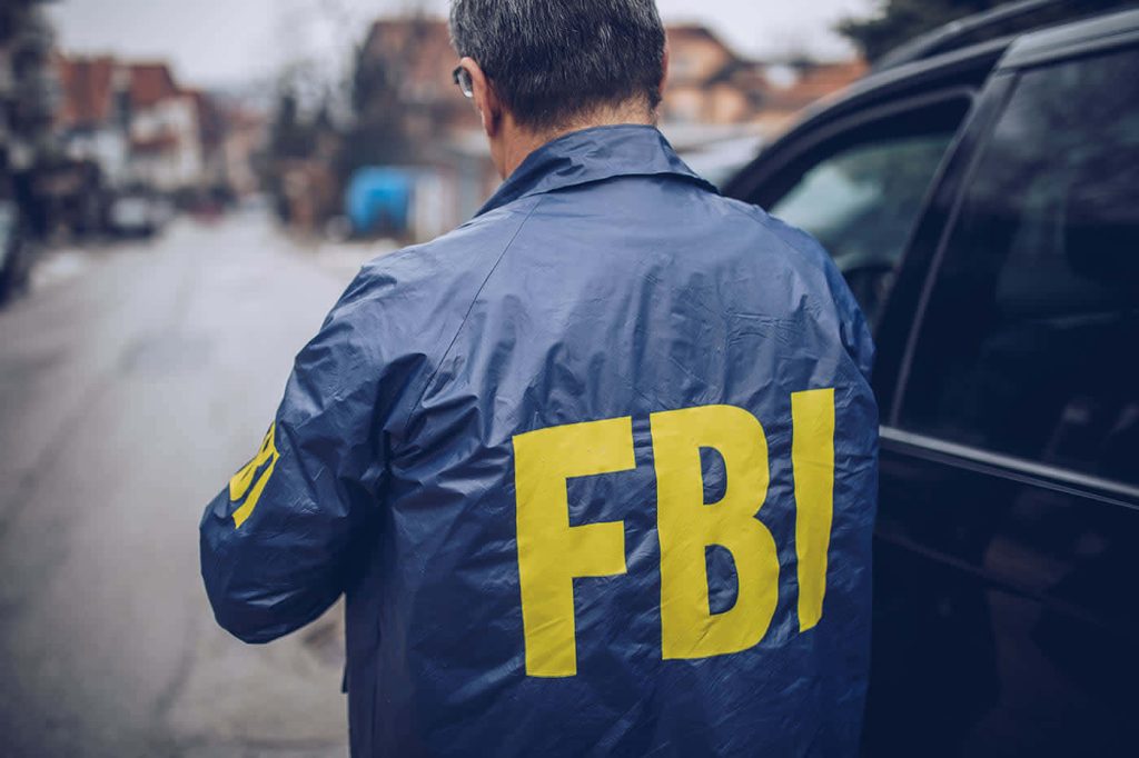 FBI agent in blue tactical jacket with yellow letters standing by vehicle on urban street background Wallpaper
