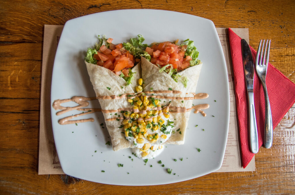 Two authentic Mexican burritos with fresh veggies and sauce on white plate rustic wooden table Wallpaper