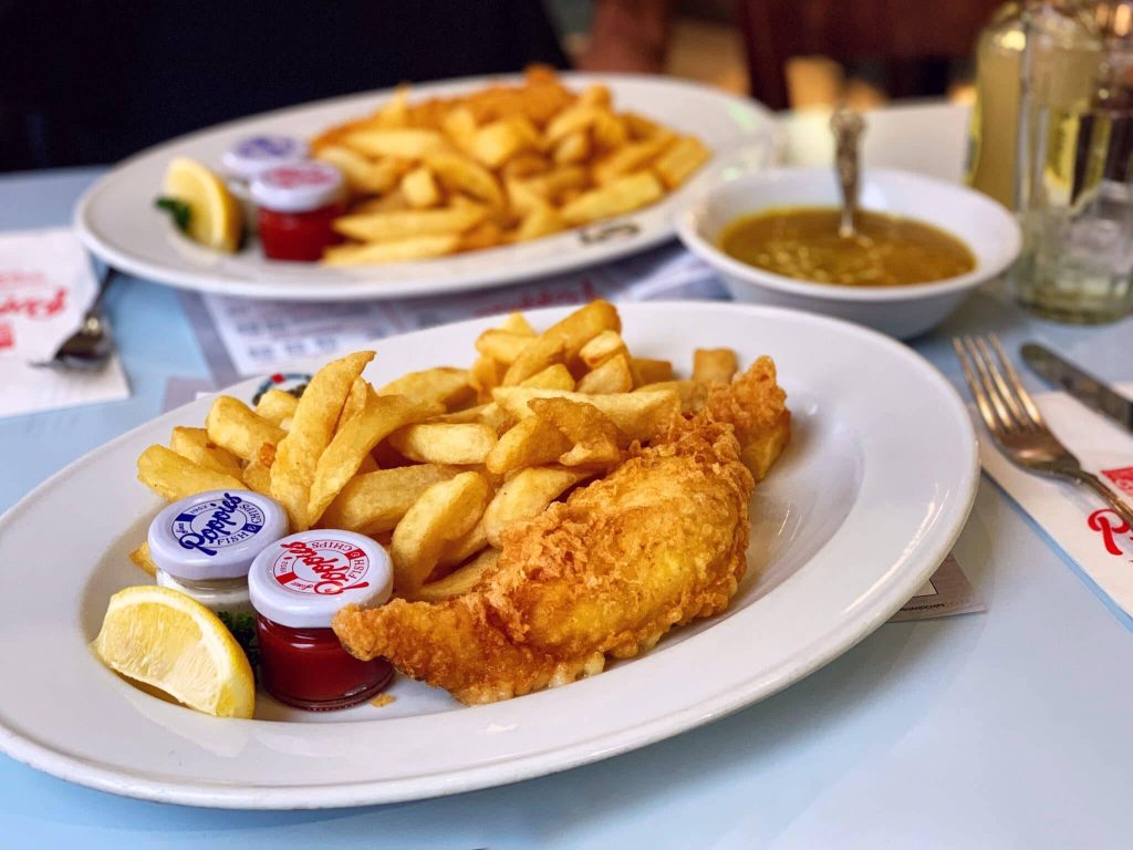 Golden crispy fish and chips with lemon and branded sauces from Poppies Fish and Chips restaurant Wallpaper