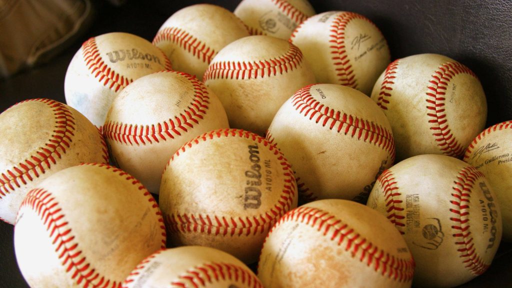 Close-up of scuffed Wilson A1010 ML baseballs with red stitching vintage leather wallpaper background