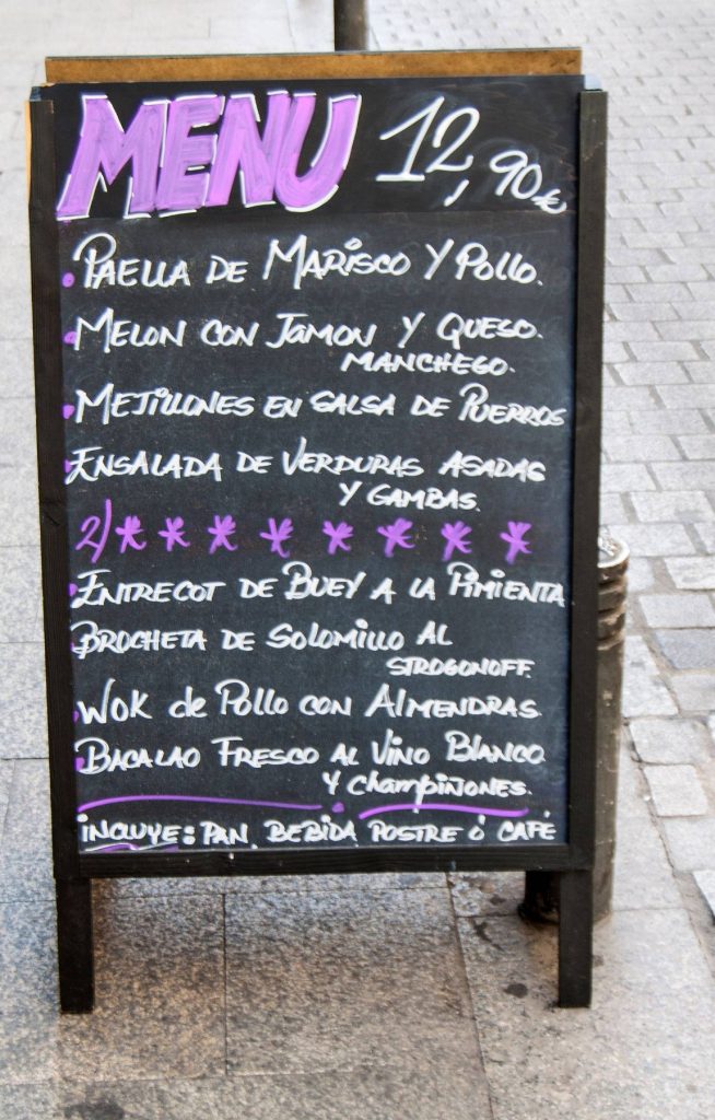 Rustic chalkboard with authentic Spanish daily menu featuring Paella and Entrecot on cobblestone street Wallpaper