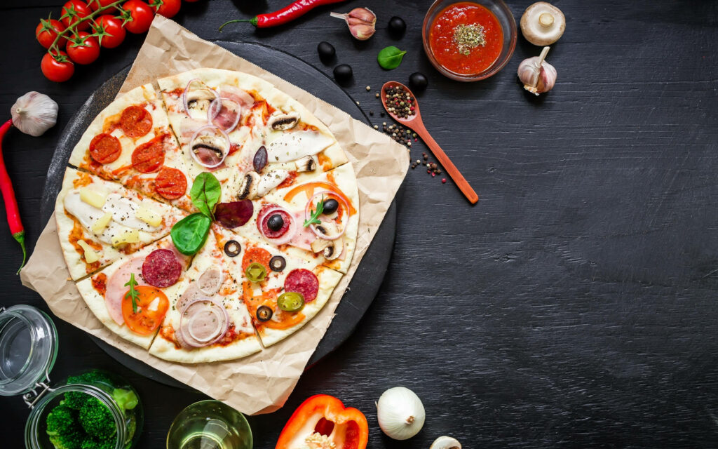 Authentic Stagioni pizza with mushrooms olives pepperoni and ham on rustic black table background Wallpaper