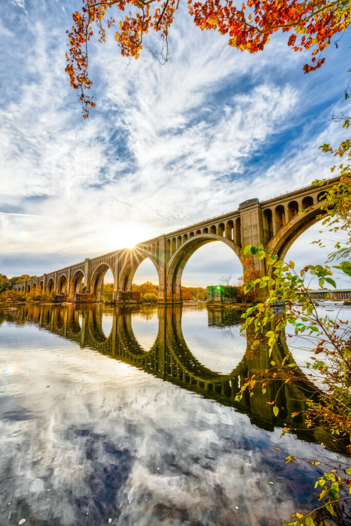 Arched bridge over calm river with autumn branches and vibrant sky reflected in water wallpaper