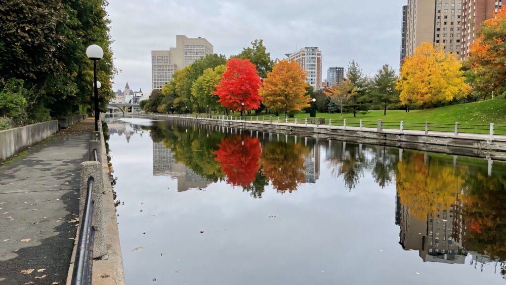 Autumn trees with red orange yellow leaves reflect on Rideau Canal Ottawa city skyline background Wallpaper