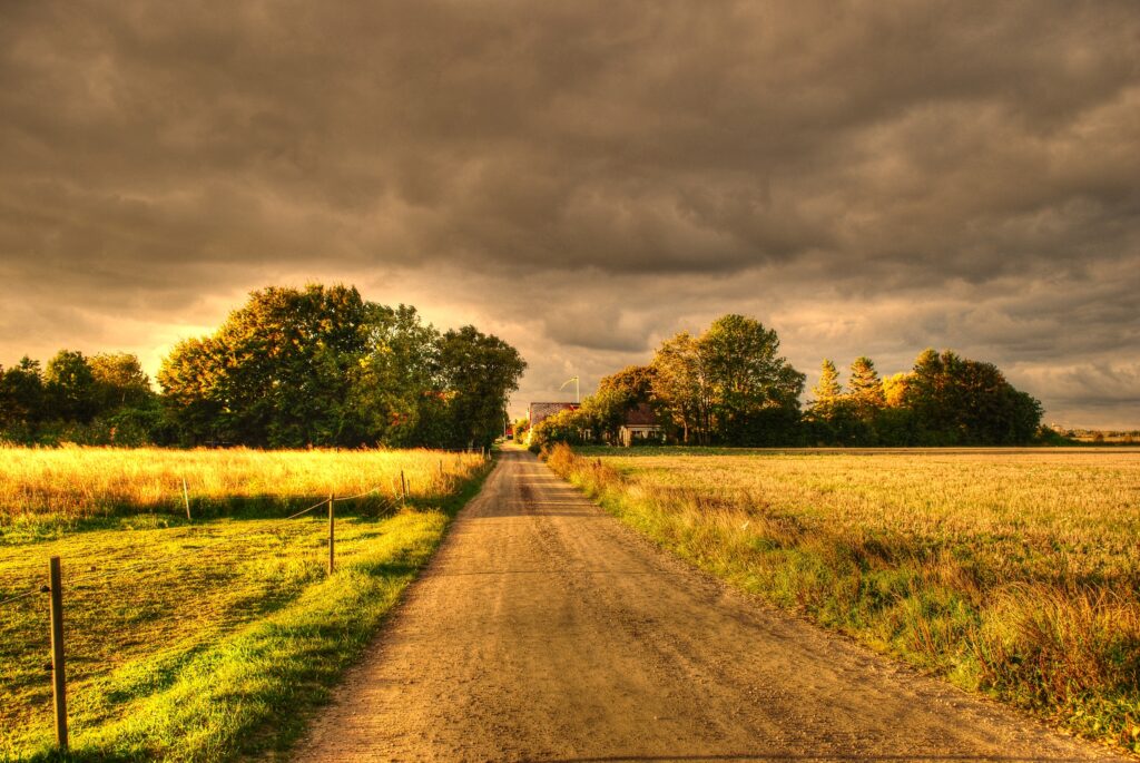 Autumn countryside road with golden fields and dramatic cloudy sky in high definition scenery Wallpaper