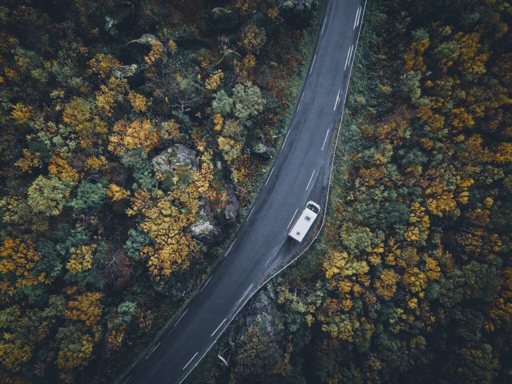 Top view winding road through vibrant autumn forest with lone car driving scenic nature wallpaper