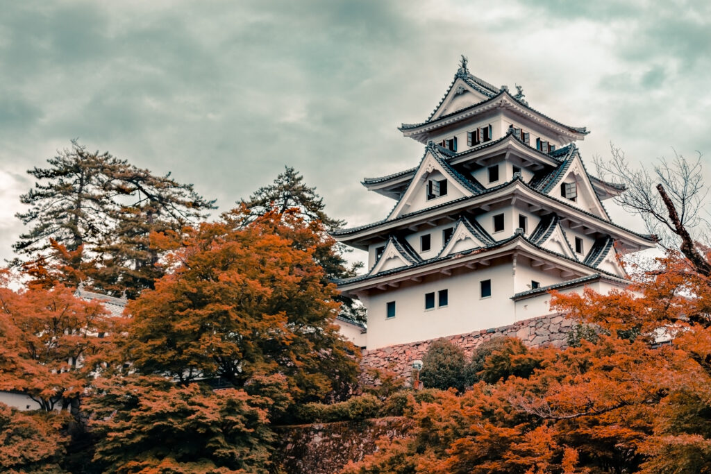 Traditional Japanese pagoda surrounded by vibrant autumn trees with dramatic cloudy sky background Wallpaper