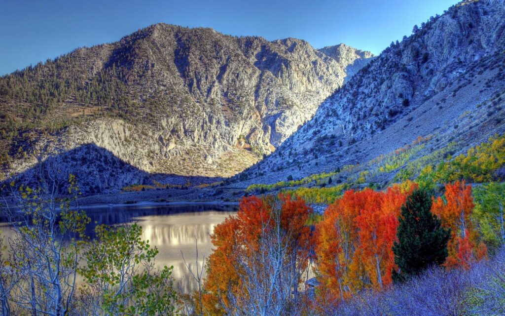 Autumn landscape wallpaper with vibrant orange red trees reflective lake and rocky mountains
