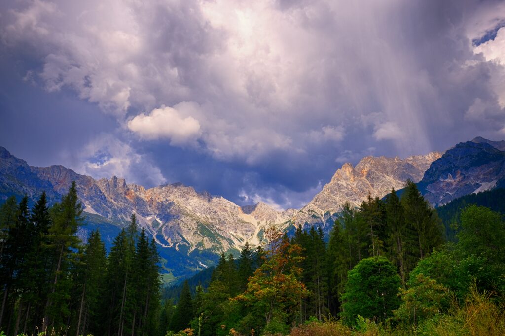 Autumn mountain landscape with rugged peaks colorful foliage dense pine trees and dramatic clouds Wallpaper