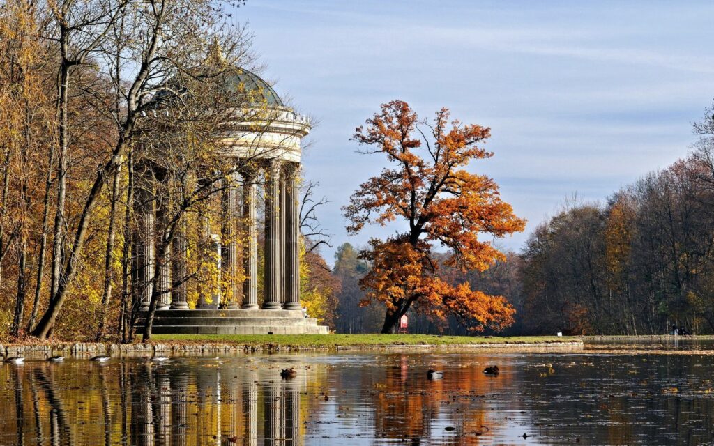 Serene autumn park with classic stone arbor and golden trees reflecting on tranquil pond water Wallpaper