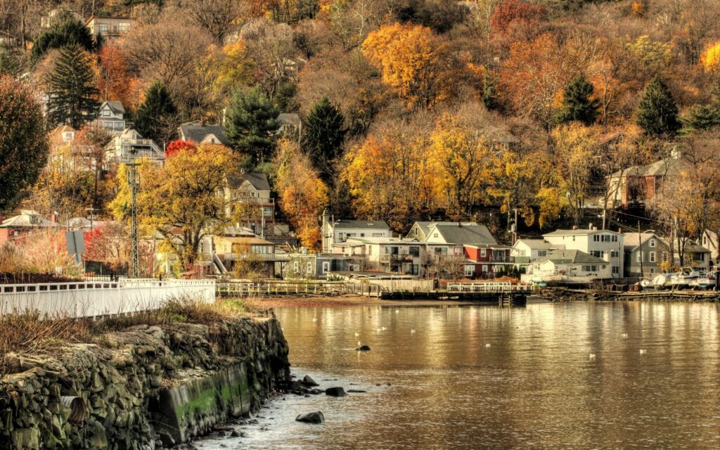 Riverside cityscape with autumn trees golden foliage calm river and docked ship wallpaper background