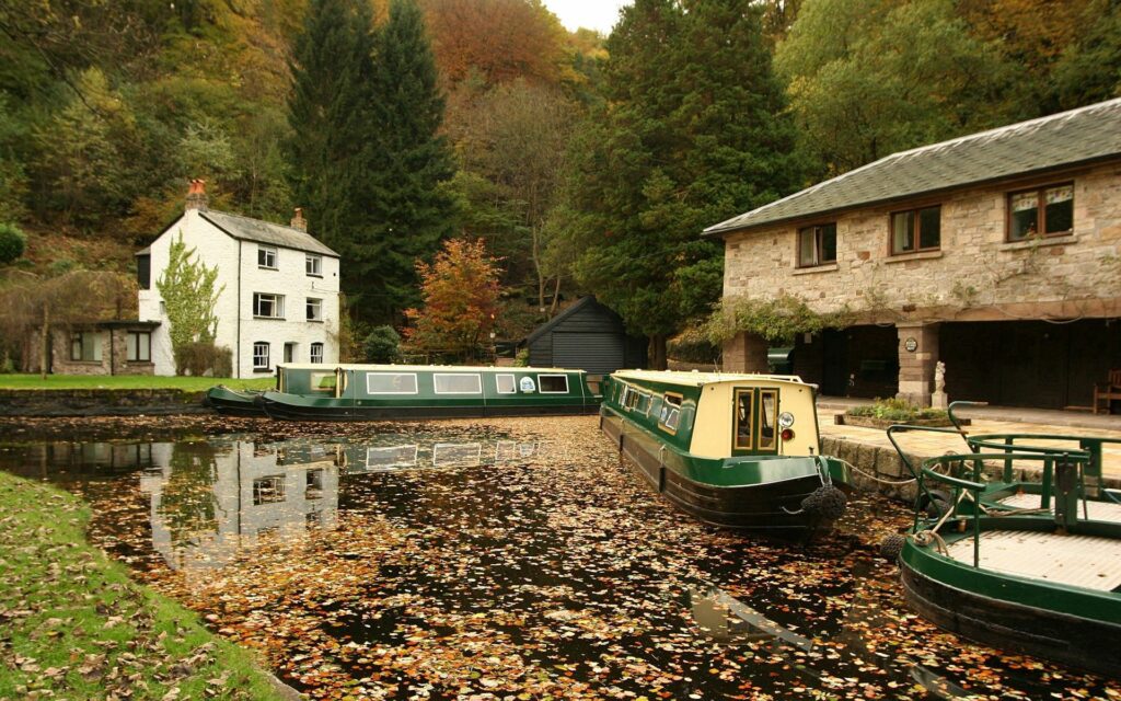 Serene riverside dock in autumn with colorful leaves canal boats rustic houses vibrant trees Wallpaper