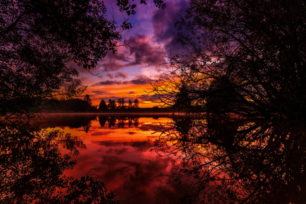 Autumn sunset over calm river with silhouetted trees reflecting orange purple and pink hues Wallpaper