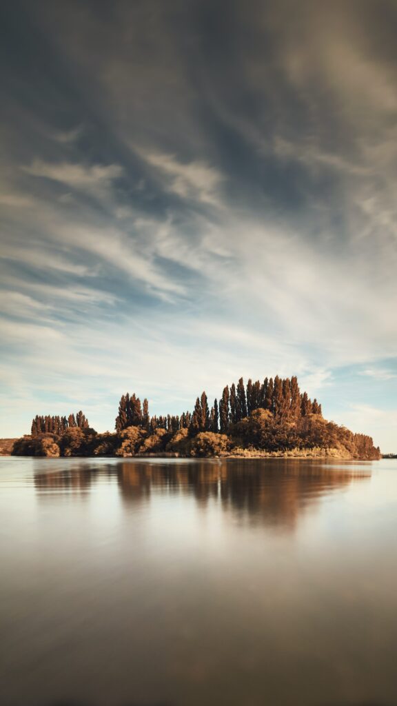 Autumn trees reflected on calm lake under dramatic clouds in peaceful dreamy natural landscape wallpaper
