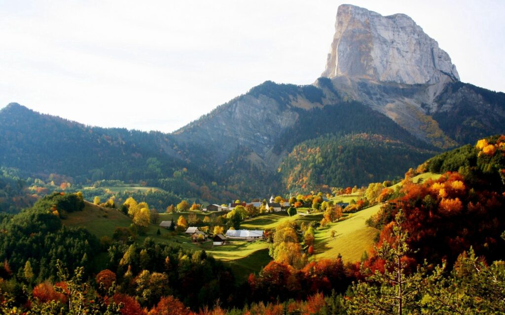 Scenic village in autumn with colorful trees rolling hills towering rock formation and mountains Wallpaper