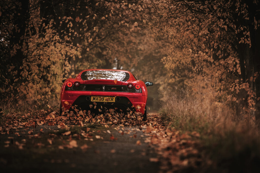Red Ferrari Scuderia on Leaf-Covered Road in Autumn Wallpaper