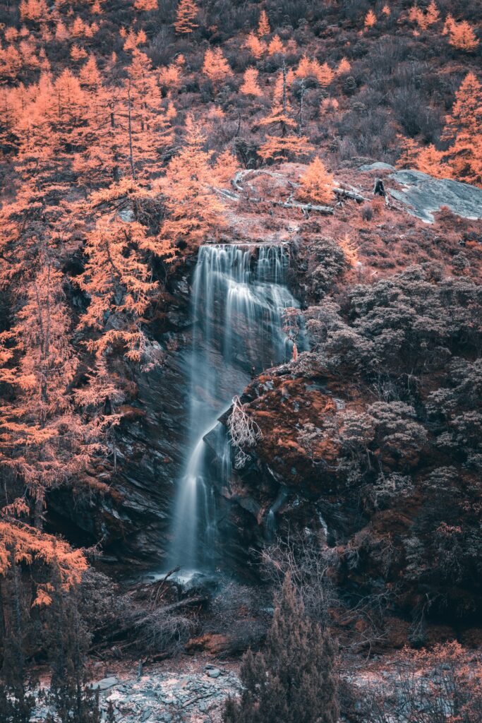 Aerial view of waterfall over dark rocks with orange autumn forest and flowing river background Wallpaper