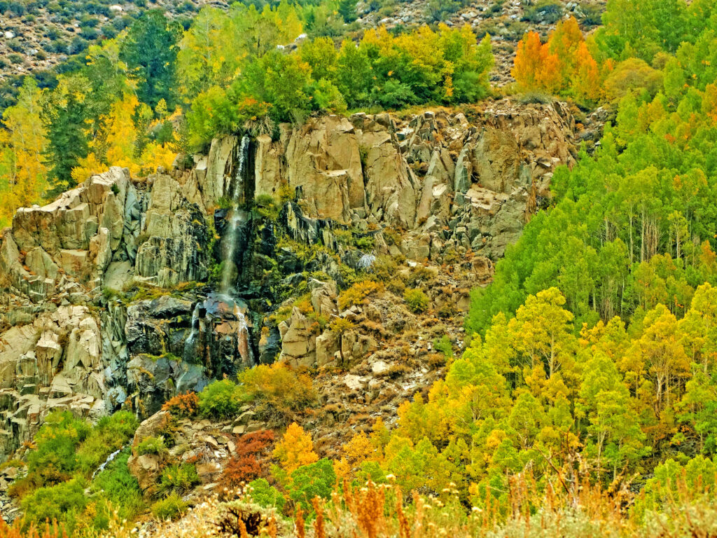 Autumn waterfall landscape with golden orange green trees cascading over rugged rocks wallpaper
