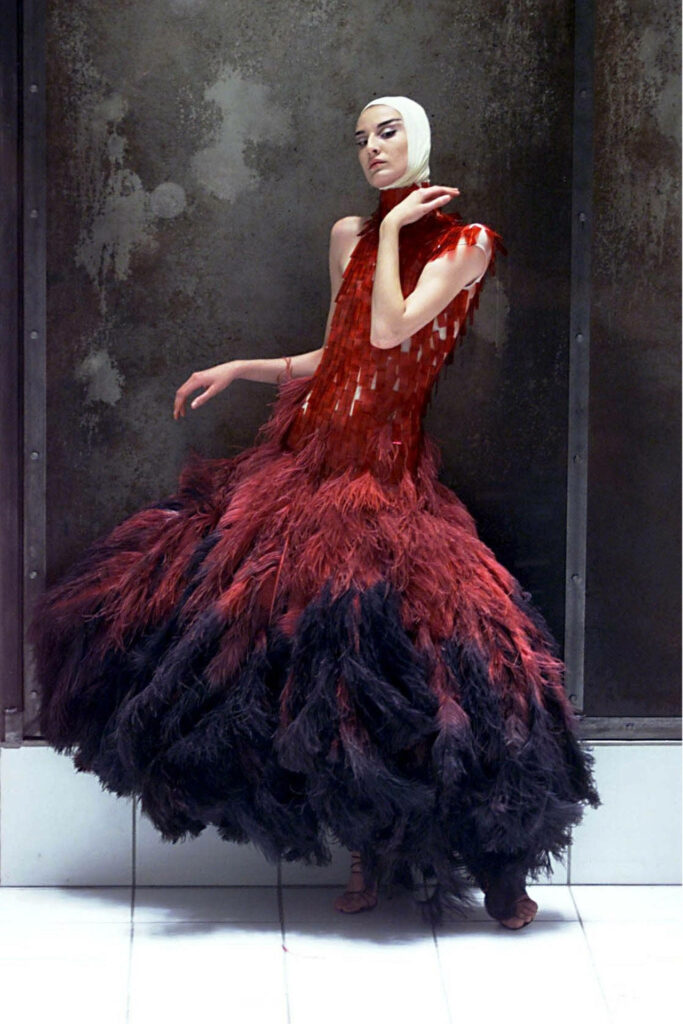 Avant-garde Alexander McQueen red ostrich feather dress with dramatic textures on industrial backdrop Wallpaper
