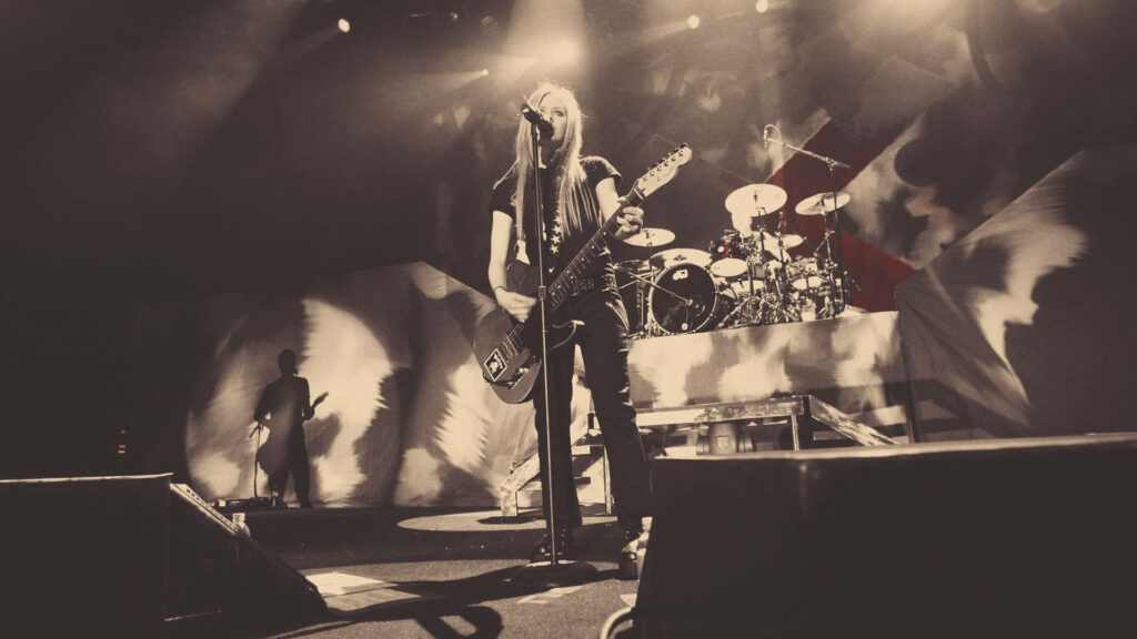 Avril Lavigne performing live on stage with guitar dramatic lighting concert energy wallpaper
