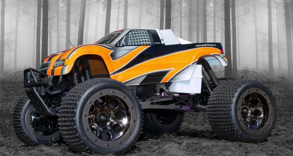 Axial Racing orange black RC monster truck with knobby tires in foggy forest off-road background Wallpaper
